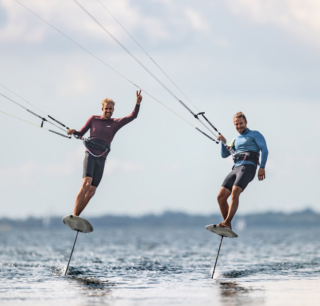 Dois praticantes de kitefoil sorrindo lado a lado sobre a água