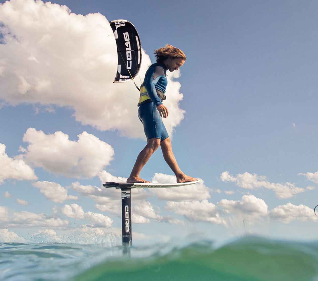 Rider standing on a foil board, flying a Core kite among the clouds